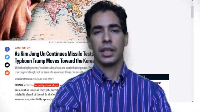 A man with dark hair in a blue striped shirt speaks in front of a blurred background featuring a map and a portion of a news article about political situations involving North Korea and the United States. Opens a new window with the video.