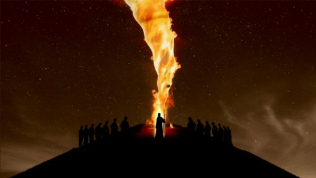 A group of silhouetted figures stands atop a hill under a starry night sky, observing a towering pillar of fire erupting from the summit. The scene evokes a profound sense of wonder akin to celestial events described in historical texts. Opens a new window with the video.