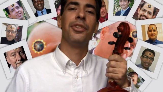 A young man in a white shirt holds a red violin, surrounded by various floating images including faces of men and celestial bodies akin to sun and planets. Opens a new window with the video.