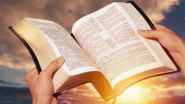 Open Bible held up against a sunset sky, illuminating the pages with warm sunlight, symbolizing enlightenment and knowledge. Opens a new window with the video.