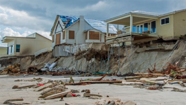 Coastal erosion has caused significant damage to seaside homes, leaving structures precariously supported on eroded cliff sides with visible debris scattered across the beach. Opens a new window with the video.