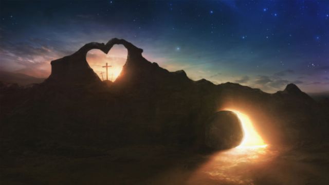 A scenic view depicting a mountainous landscape at twilight with an archway shaped naturally like a heart framing a cross at its center. A radiant celestial body rises from the horizon, casting a warm glow under a sky dotted with stars. Opens a new window with the video.