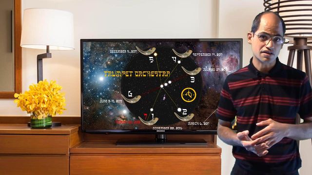 A man in a striped shirt stands next to a wooden television stand in a living room. On the TV screen is a depiction of celestial constellations associated with the Mazzaroth, displayed in a circular arrangement, intertwined with specific temporal markers and symbols. Opens a new window with the video.