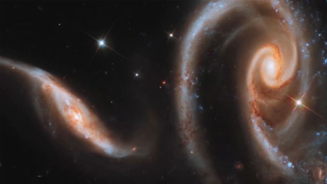 A vivid image of several galaxies interacting in deep space, featuring swirling arms of stars and glowing centers surrounded by cosmic dust and bright star formations. Opens a new window with the video.