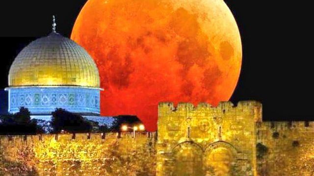 A large, reddish moon looms spectacularly behind the Dome of the Rock in Jerusalem, with ancient stone walls in the foreground under a night sky. Opens a new window with the video.