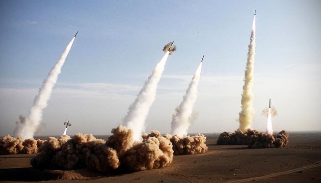 Multiple rockets launching simultaneously from a desert base, creating thick trails of smoke and dust against a clear sky. Opens a new window with the video.