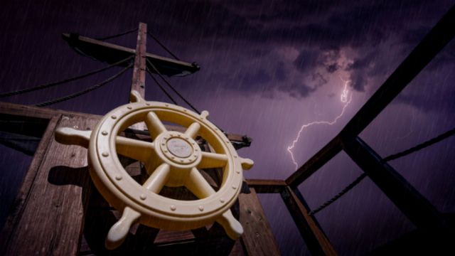 A ship's helm in the foreground with a dramatic background featuring a lightning bolt cutting through dark, stormy skies at night. Opens a new window with the video.