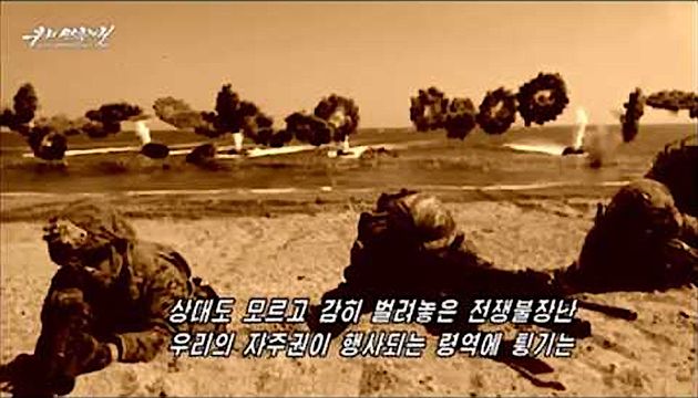 Sepia-toned image of soldiers in prone positions taking cover, with aircraft and explosions evident in the background, illustrating a historical military operation. Opens a new window with the video.
