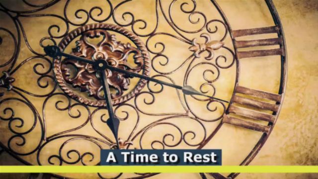 An ornate clock featuring wrought iron details and Roman numerals, with its hands pointing to eleven and two. The design includes swirling patterns and a central emblem resembling a flower. The upper part of the image contains text &ldquo;A Time to Rest&rdquo; on a semi-transparent yellow strip. Opens a new window with the video.