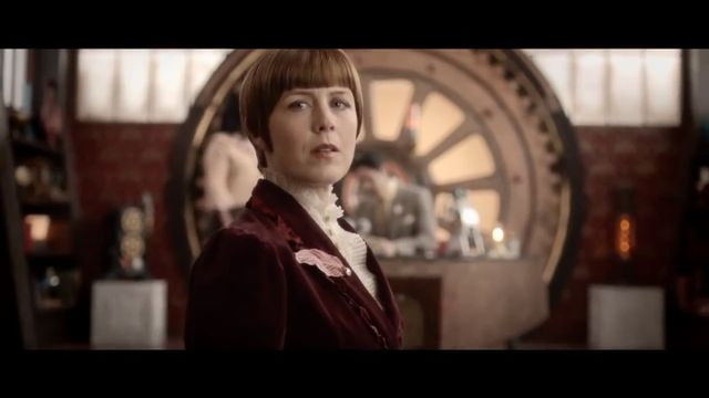 A woman with a short brown bob haircut and a burgundy blazer stands confidently in an ornate room filled with antique furniture and circular, metallic artifacts resembling astronomical instruments around the walls. The background gives a classical yet mystical ambiance reminiscent of a study dedicated to the Mazzaroth. Opens a new window with the video.