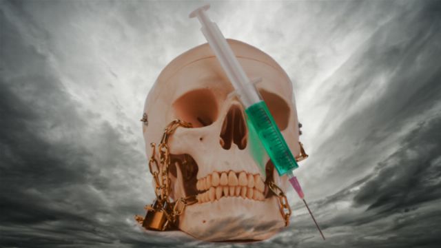 A surreal image featuring a human skull with gold chains hanging from it, pierced by a large green syringe against a dramatic cloudy sky. Opens a new window with the video.