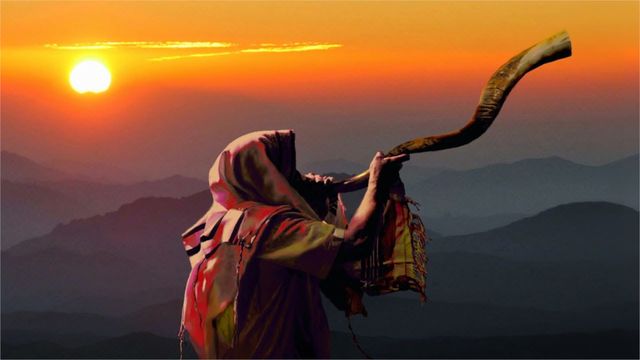 An ancient figure in traditional robes stands on a mountain peak at sunrise, blowing a long shofar towards the rising sun, with layers of mountains fading into the horizon beneath a vibrant orange sky. Opens a new window with the video.