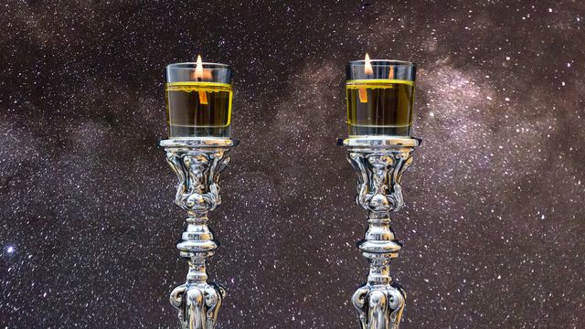 Two ornate silver candleholders with lit candles against a backdrop of a star-filled sky, suggesting a celestial celebration or reflection. Opens a new window with the video.