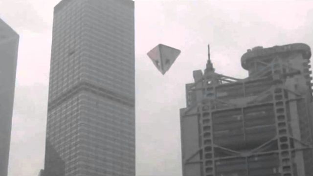 A grayscale image of a large metropolitan skyline, featuring modern high-rise buildings under an overcast sky, with an origami-style kite flying amidst the buildings. Opens a new window with the video.