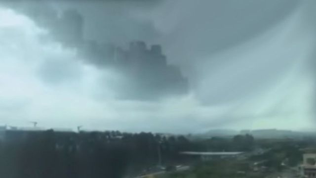 A vast cloudscape depicts towering cumulus clouds and a sweeping view of an urban area, possibly early in a storm cycle, with varying shades of gray dominating the sky. Opens a new window with the video.