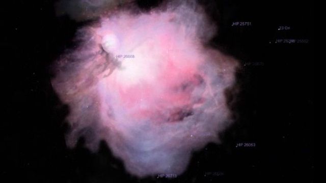A celestial nebula illuminated in hues of pink and white, surrounded by darkness, with stars pinpointed by their astronomical catalog numbers. Opens a new window with the video.