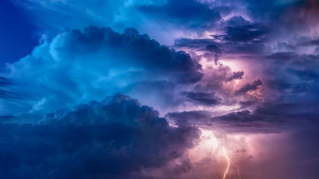 A dramatic stormy sky with vivid lightning illuminating cumulus clouds. Hues of deep blue and purple envelop the atmosphere, showcasing the grandeur of creation. Opens a new window with the video.